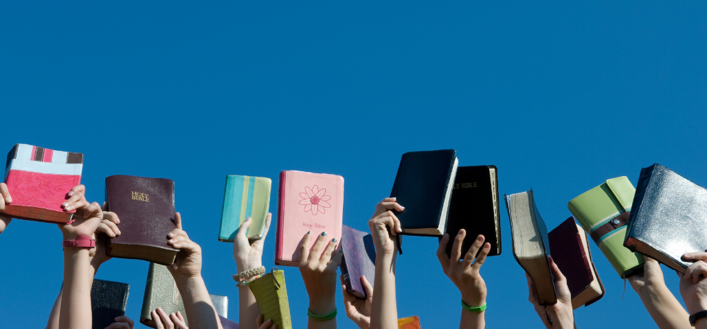 Many hands holding up Bibles.
