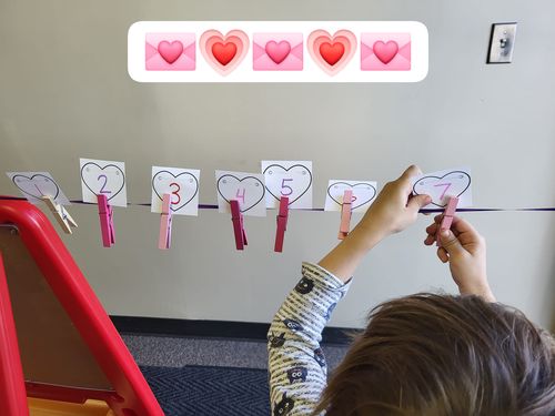 Child attaching hearts to a ribbon with a clothespins.