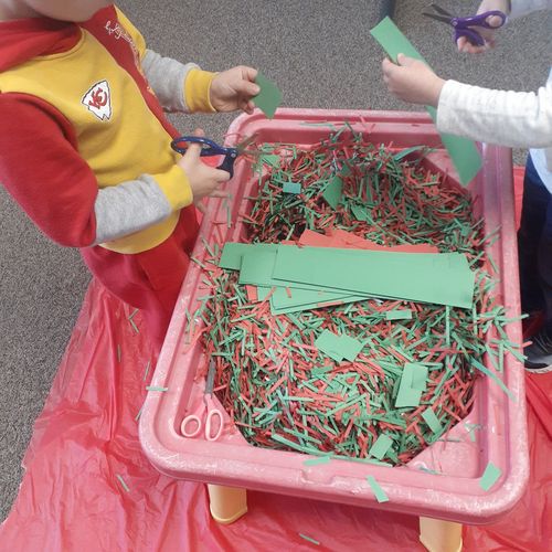 Children cutting thin strips of paper into a sensory table.