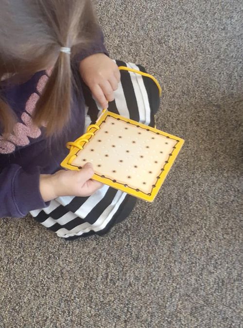 Child threading and wrapping a string on a piece of cardboard with a grid of holes.